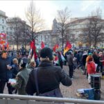 Persone con bandiere comiciano manifestazione in Piazza Scala, davanti a Statua di Leonardo da Vinci e Teatro Scala.