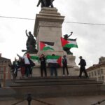 Persone che sventolano bandiere palestinesi in cima alla statua in Milano.